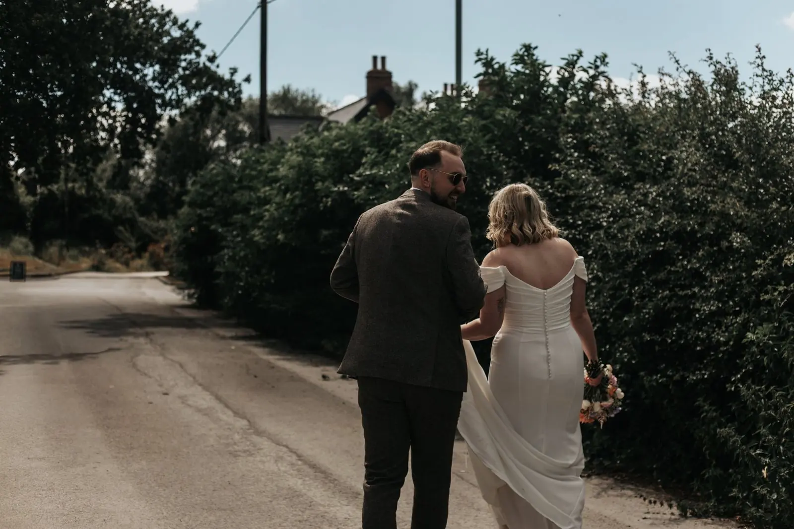 Couple walking down a country lane with the groom laughing back at his bride