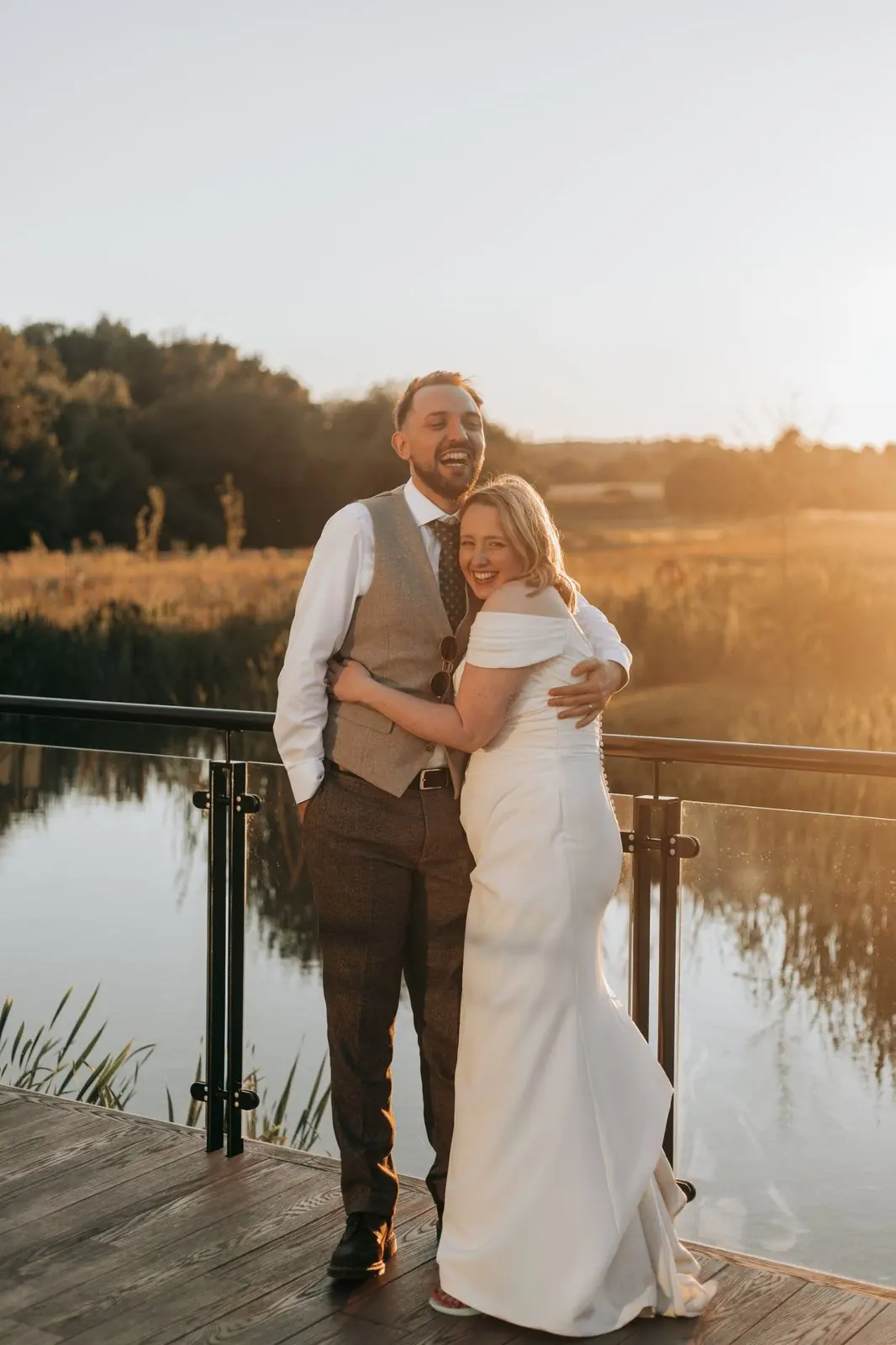 Couple hugging and laughing on a lakeside deck at golden hour