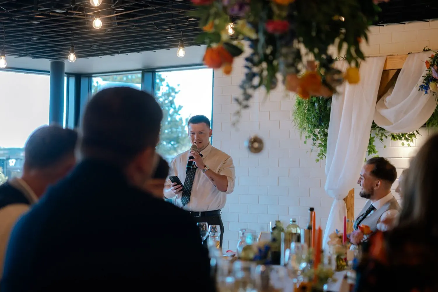 Best man giving a speech at the wedding reception while the groom laughs