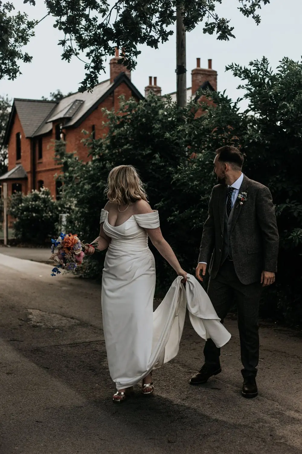 Bride holding her dress train and bouquet while the groom looks back at her