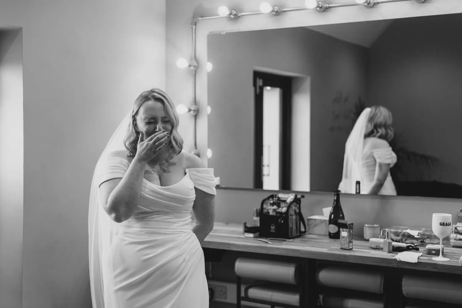 Bride laughing with her hand over her mouth while getting ready, in black and white