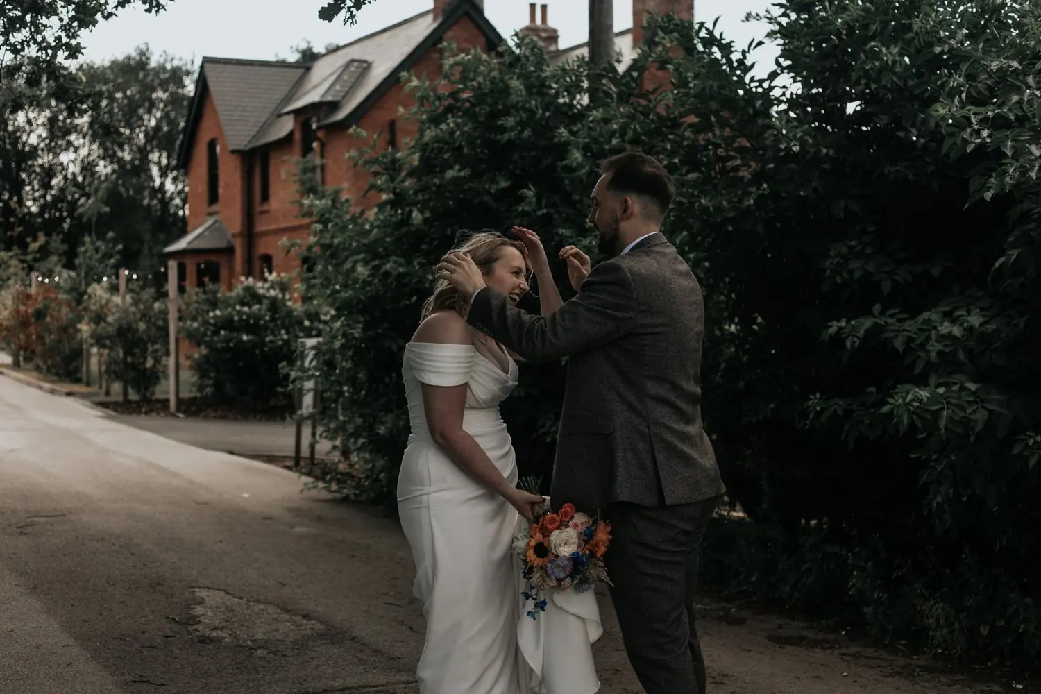 Couple laughing together in front of a red brick building, the bride holding her bouquet