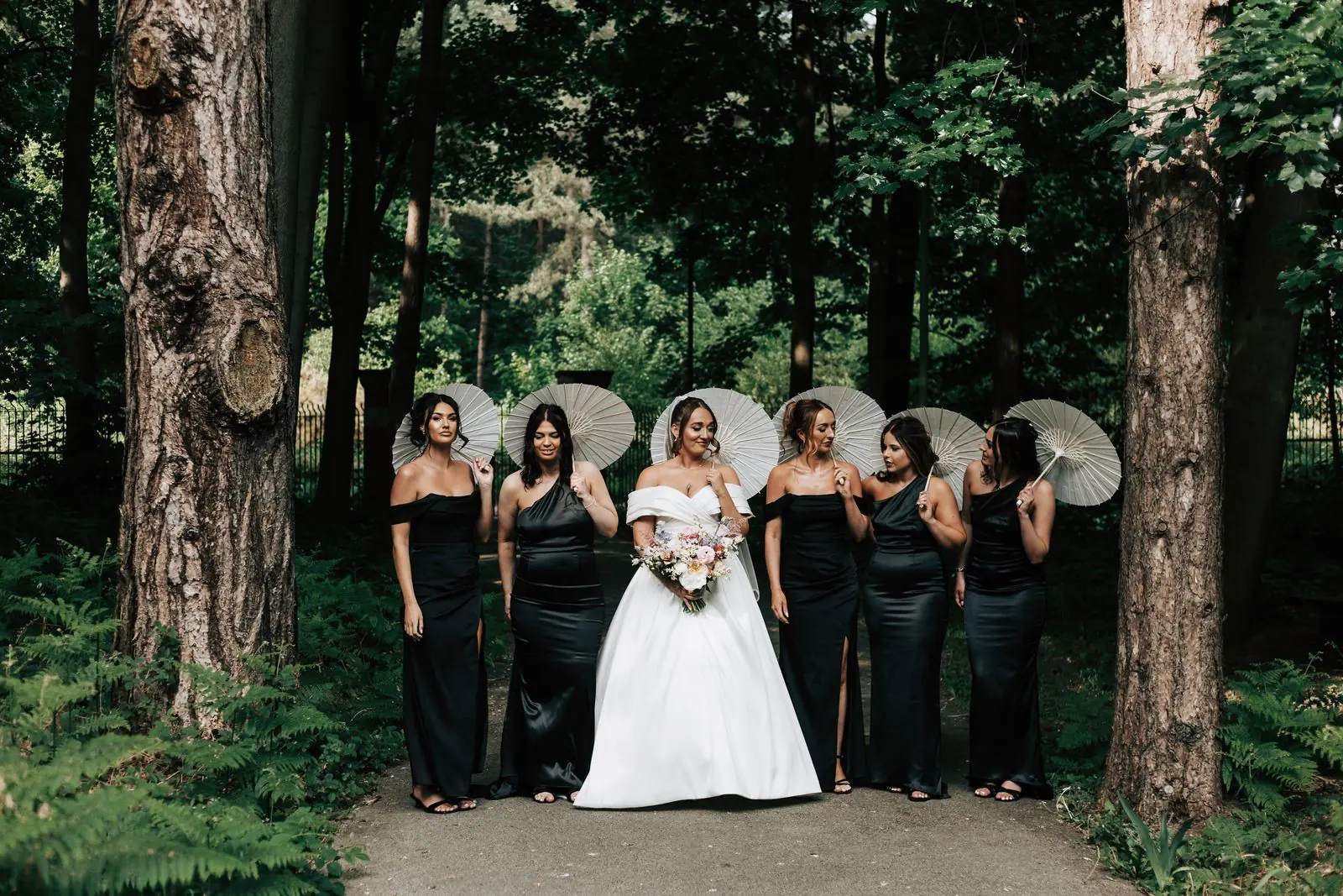 Bride and bridesmaids with parasols among tall trees