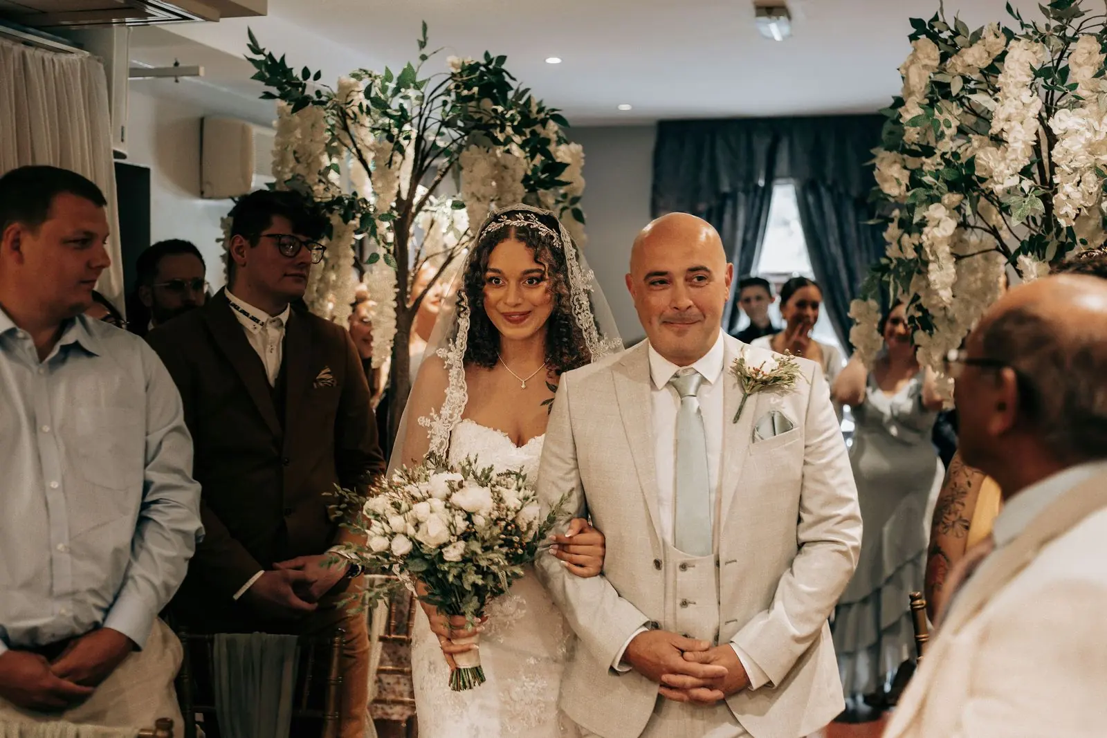 Father walking the bride down the aisle past floral arrangements