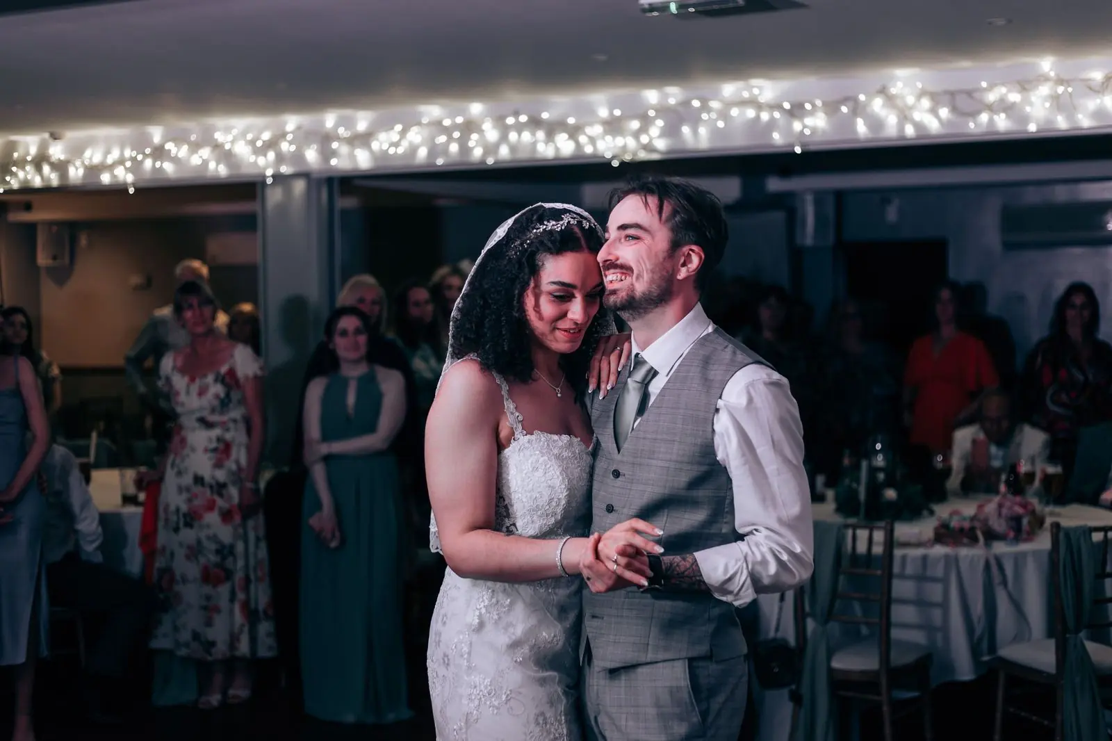 Couple smiling during their first dance under fairy lights