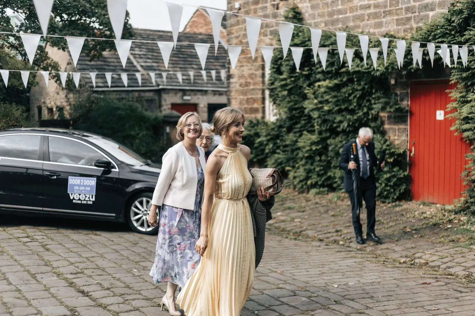 Guests arriving in the cobbled courtyard under bunting with a car behind them