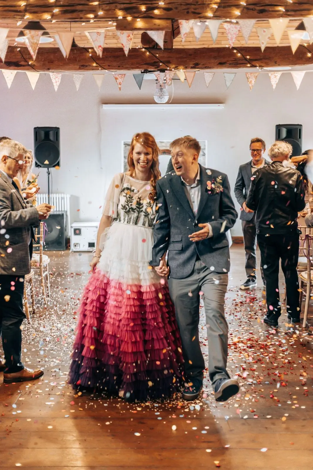 Couple laughing as they walk up the aisle in a shower of confetti