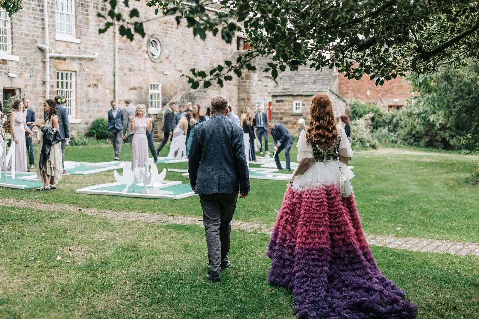 Bride in her ombré skirt walking across the lawn towards guests playing crazy golf